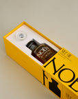 A sleek yellow box containing a bottle of Noén Nile Oil, a luxurious body oil. The intimate oil is housed in a minimalist glass bottle with a wand applicator, making it easy to use. This indulgent product is formulated with a blend of natural ingredients, including beta-caryophyllene, calendula, moringa, buriti fruit, and rosemary, to soothe, rejuvenate, and revitalize the skin.