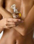 A woman's hand holding a bottle of Noén's Nile Afterplay Oil, a luxurious intimate oil. This indulgent product, formulated with a blend of natural ingredients, is perfect for soothing and rejuvenating the skin after intimate moments, including sex, but also for whole body hydration.