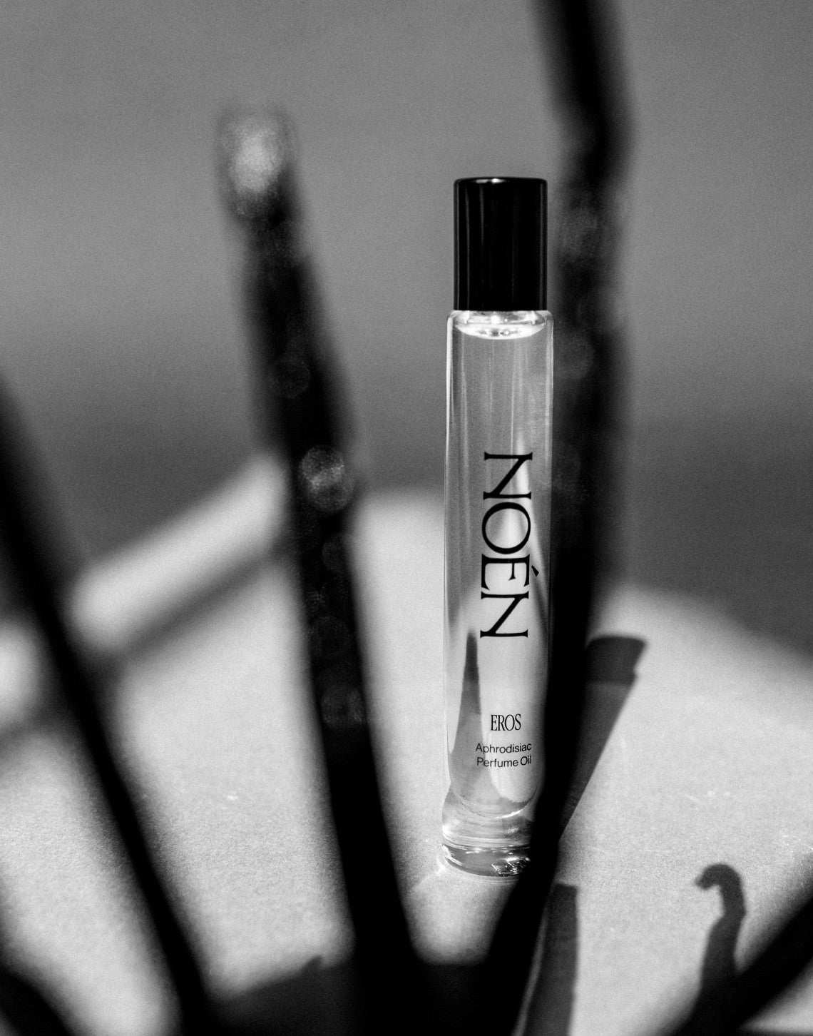 Eros Perfume Oil roll-on in black and white among dried stems