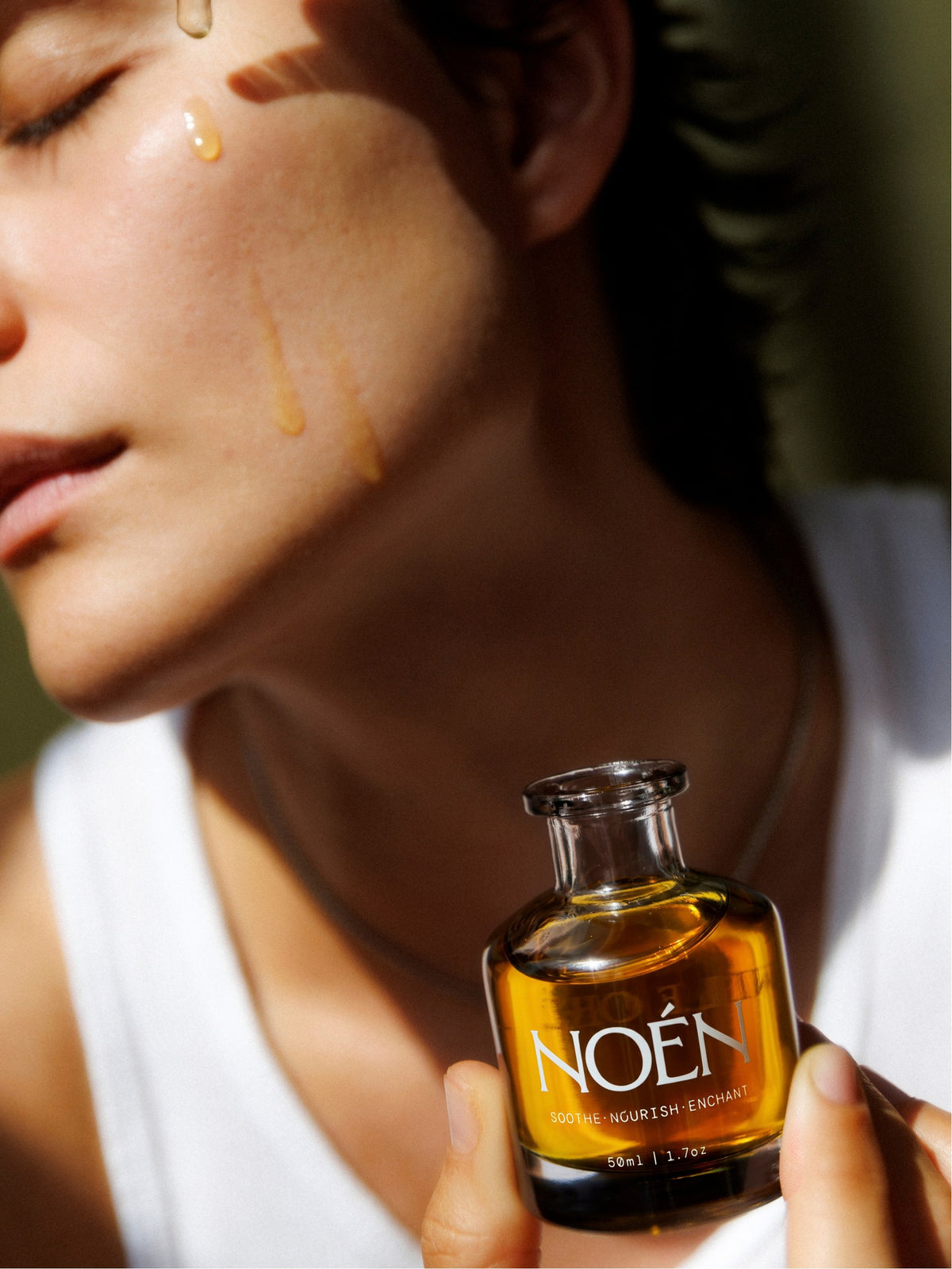 Woman with a drop of Nile Oil on her cheek, holding the bottle