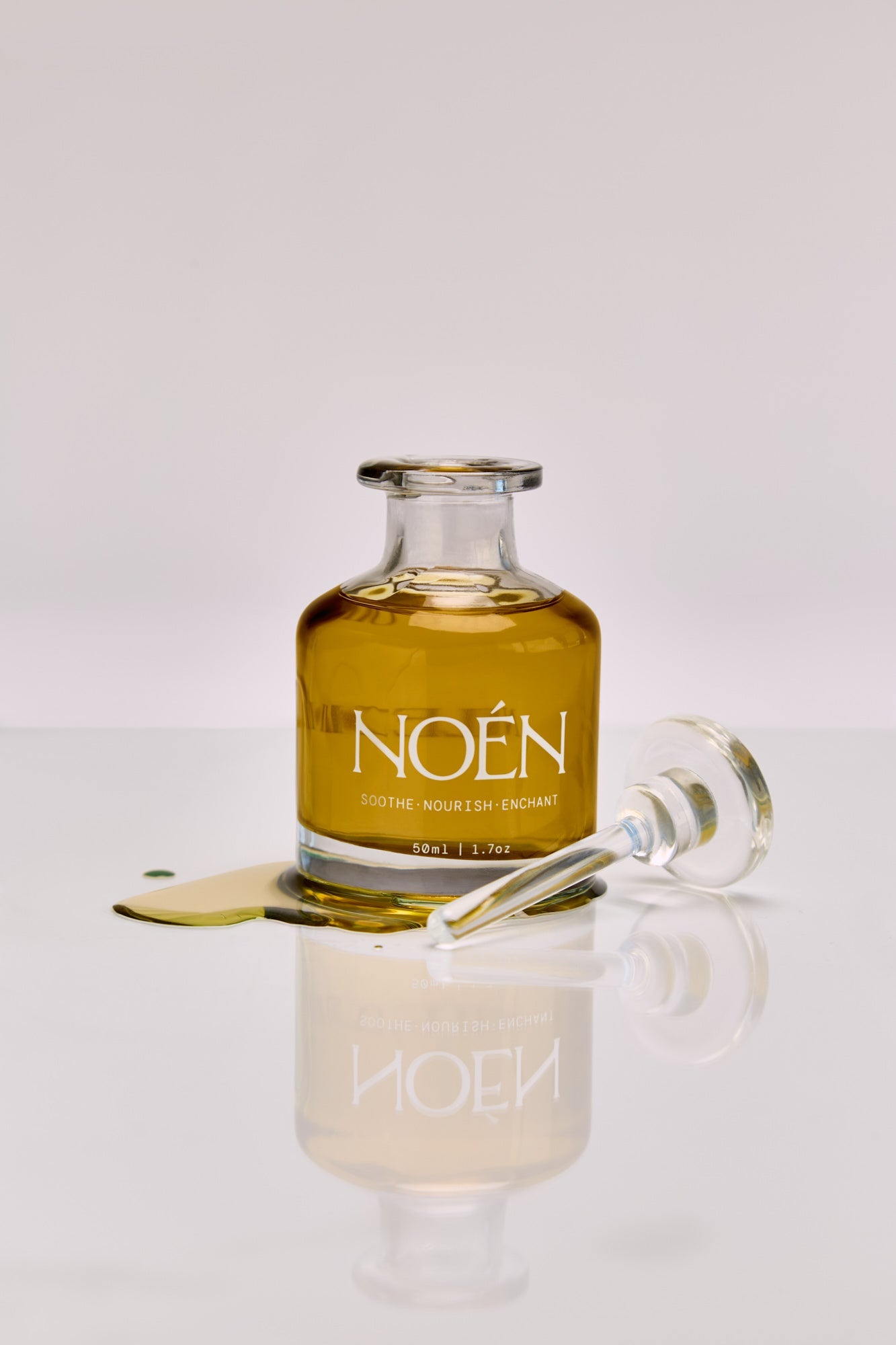 NOÉN Afterplay Oil bottles with organic golden oil, illuminated by sunlight. This luxury, cruelty-free blend with jojoba, calendula, and buriti oil hydrates, soothes, and revitalizes sensitive skin for a soft, nourished, and refreshed fee