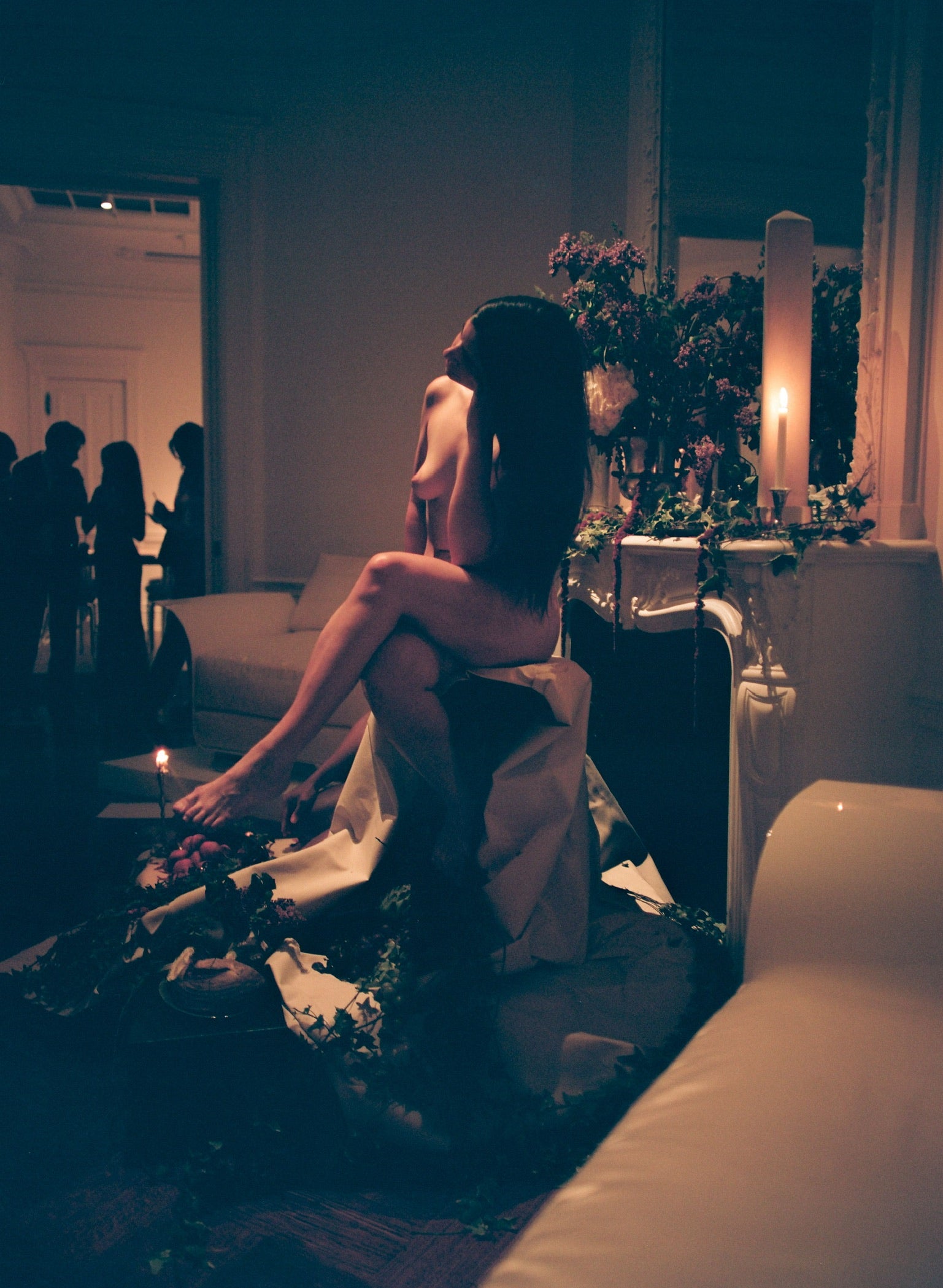 Woman sitting on a couch in a dimly lit room with candles and floral arrangements.